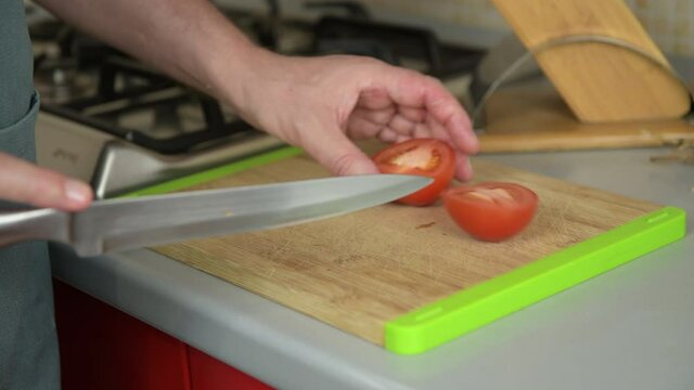 Authentic male hands cutting tomato on a cutting board in the kitchen for prepare the friselle, tipical apulian dish, dry bread with tomatoes, oregano and olive oil