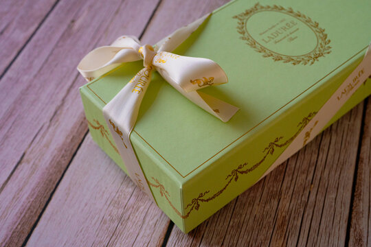 Nice, France - 18.06.2021: Famous French Macaroons from Laduree store. A green special gift box on a wooden background. Assorted Laduree Macaroons in the gift box. High quality photo