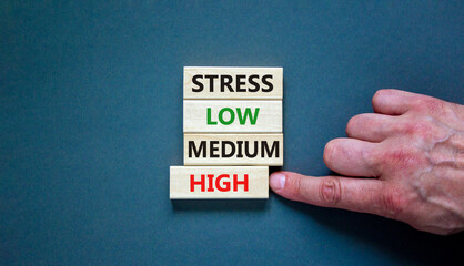 Low or high stress level symbol. Businessman chooses the wooden block with words high stress. Words stress low medium high. Beautiful grey background. Low or high stress level concept. Copy space.