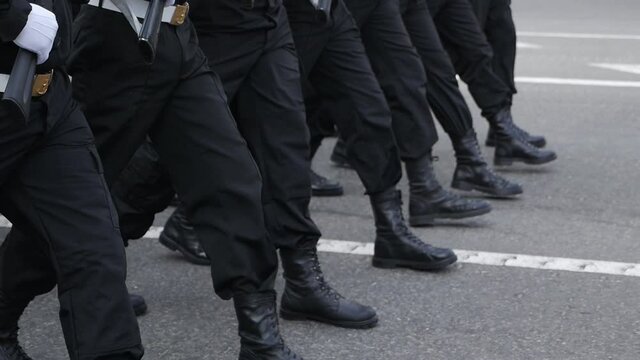 The marching legs of a group of men in blue uniforms during an afternoon parade on the street.slow motion