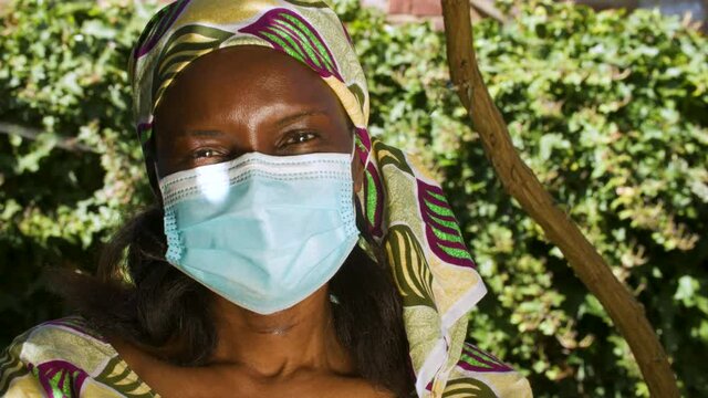 Middle aged African woman outside wearing traditional clothes and a face mask during COVID-19 Coronavirus pandemic in Africa