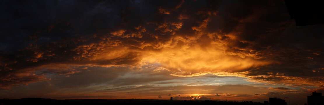 High resolution stormy sunset panorama. Epic clouds highlighted gold by setting sun.