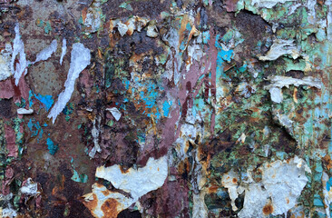 The texture of a rusty metal wall surface with paint residues and scraps from ads