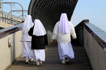 Rear view of three unrecognizable nuns walking in a pedestrian street.