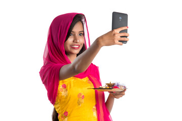 Beautiful young happy girl taking selfie with pooja thali using a mobile phone or smartphone on a...