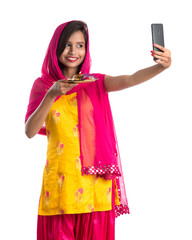 Beautiful young happy girl taking selfie with pooja thali using a mobile phone or smartphone on a...