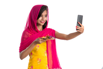 Beautiful young happy girl taking selfie with pooja thali using a mobile phone or smartphone on a...