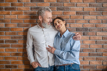 A gray-haired man hugging his wife while standing near the brick wall