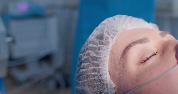 Close-up a female patient in a disposable hat and in the nose is an anesthesia tube.