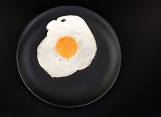 Fried egg lies on a black plate on a black background