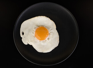 Fried egg lies on a black plate on a black background
