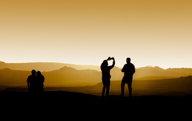 Silhouette of two tourists taking photos of each other at a mountain scene during golden sunset