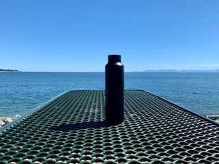 Black drinking container on a green picnic table over the sea, summertime, outdoor  