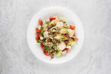 Salad with mussel, shrimp, tomato cherry, cucumber, zucchini pasta, microgreen, yogurt sauce on white plate on light table.