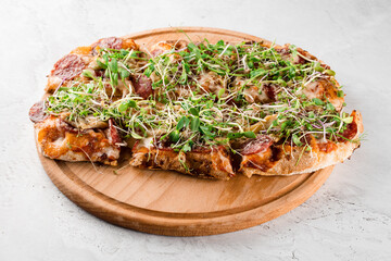 Pinsa romana with salami, cheese, mushrooms, decorated with microgreens on wooden boardon white background.