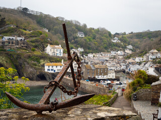 An anchor in the foreground overlooking boats moored in the harbour at the coastal village and 12th century port of Polperro on the south coast of Cornwall, UK. 