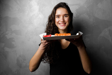 Girl holding philadelphia rolls in a paper box on gray background. Sushi, food delivery.