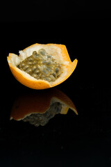 Single granadilla fruit shot on black reflective surface with reflection showing, seeds inside...