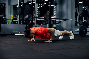 Fototapeta na wymiar Shot of a muscular and strong guy doing push-ups in a darkened gym with mirrors. Exercise for the whole body, plank workout, sport