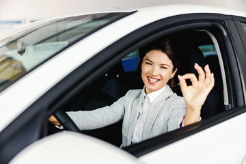 Smiling woman sitting in the car she wants to buy and sowing okay sign. Car salon interior.