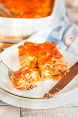 Slice of delicious beef lasagne with cheese crust on a white plate viewed close up on the side showing the layers.Restaurant menu, recipe