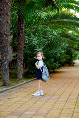 Fototapeta na wymiar a little girl, a schoolgirl, goes to school on the street with a denim backpack, and in a medical mask