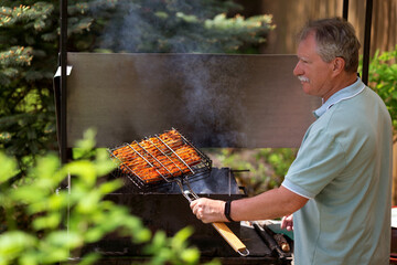 Senior man grilling in the backyard of his country house in sunny summer day.