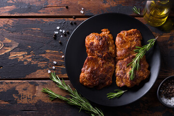 Fried vegan soy steak with rosemary, salt and pepper on black plate on wooden background, free space