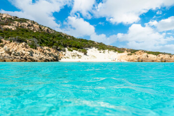 (Selective focus) Defocused white sand beach in the background bathed by a beautiful turquoise sea in the foreground. Isola di Spargi, Maddalena Archipelago, Sardinia, Italy.