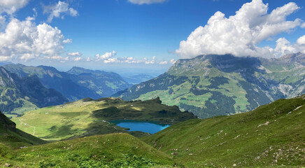 Fototapeta premium Beautiful lake surrounded by high mountains. Landscape in the swiss alps. Gorgeous green peaks with a blue sky in the background. 