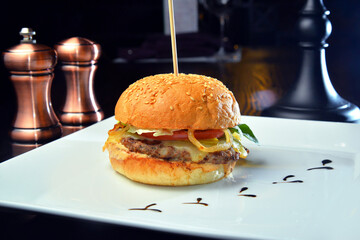 Close-up of delicious fresh home made burger with lettuce, cheese, onion and tomato on white plate on a dark background