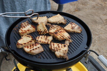 Marinated Grilled Philippine Pork on a Small Gas Grill with Grill Stripes and Tongs Roasting in a Campgrounds