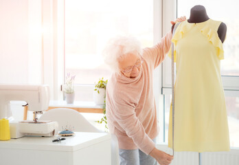 mature woman measuring dress on mannequin in atelier