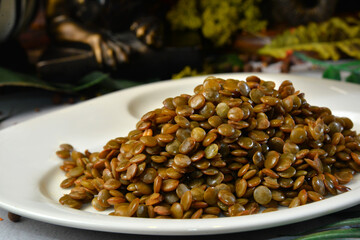 White plate with brown cooked lentils on decorated background. - Image Vegetarian food
