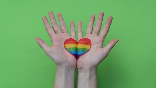 Open hands with rainbow LGBT heart over green background. LGBTQ right concept. LGBT equality symbols.