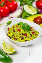 Bowl of Avocado Guacamole Mexican Dip with Avocado, Lime, Tomato, Cilantro with Fresh Ingredients on a Table with Tortilla Chips. Selective focus.