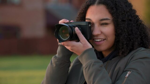 Beautiful African American mixed race biracial teenager young woman using a digital camera outside in golden sunlight taking photographs