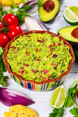 Bowl of Avocado Guacamole Mexican Dip with Avocado, Lime, Tomato, Cilantro with Fresh Ingredients with Tortilla Chips. Selective focus.