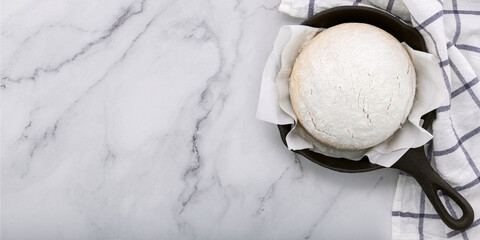 Fresh raw homemade yeast dough resting in cast iron skillet on marble table flat lay.