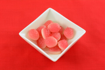 Strawberry gummy candy in shape of strawberry fruit in white candy dish on red background