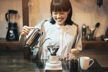 照明の落ち着いた空間で、ハンドドリップでコーヒーを淹れる若い女性
