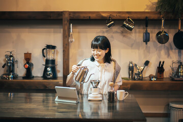 照明の落ち着いた空間で、ハンドドリップでコーヒーを淹れる若い女性