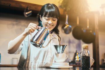 照明の落ち着いた空間で、ハンドドリップでコーヒーを淹れる若い女性