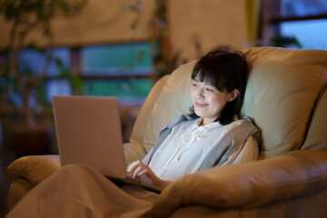 ひかえめな照明の部屋のソファで、ノートパソコンを使う若い女性