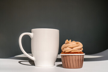 A cupcake or muffin stands next to a cup of coffee.