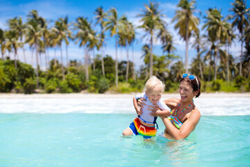 Mother and baby on tropical beach. Kids swim.