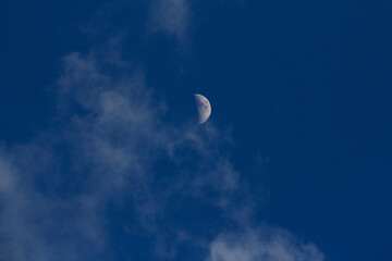 Moon in metallic blue sky with clouds