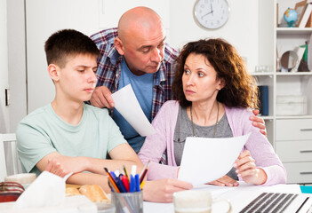Obraz premium Parents with teenager son reading and writing some documents at home table ..