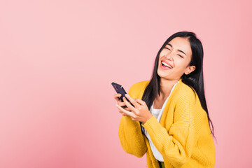 Happy Asian portrait beautiful cute young woman excited laughing holding mobile phone, studio shot isolated on pink background, female using funny smartphone making winner gesture