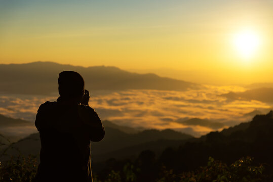 silhouette of photographer taking a beautiful picture of landscape during sunset period on the view point
